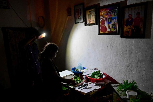 A man use a mobile phone torchlight as a woman works with plants at their home in Colombo on October 19, 2026 during a power outage as part of Sri Lanka's electricity rationing measure, two days after a nationwide blackout. Sri Lanka announced nationwide electricity rationing from October 19, two days after a complete breakdown of the national grid caused by a fault at a coal-fired generator. The state-run electricity utility said power would be cut for one hour in stages across the island during a four-hour period from October 19 evening. (Photo by Ishara S. KODIKARA / AFP)