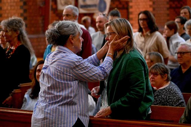 People embrace during a vigil for Australian politician Helen Haines at the Holy Trinity Cathedral in the northern regional city of Wangaratta, some 250 kilometres north-east of Melbourne on October 20, 2026. Australian lawmaker Helen Haines has lost a leg after being struck by a car in a deliberate attack, local media said October 20. (Photo by William WEST / AFP)