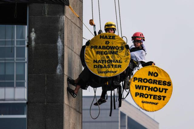 Greenpeace Indonesia activists hanging from the Welcome Statue at the Hotel Indonesia Roundabout hold protest signs in Jakarta on October 20, 2026. The demonstration on the second anniversary of President Prabowo Subianto's inauguration urged the government to tackle the worsening climate crisis and the rising cost of living. (Photo by BAY ISMOYO / AFP)