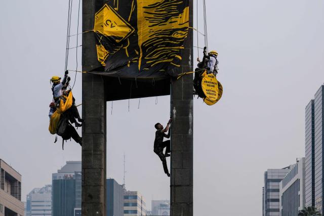An Indonesian military personnel climbs up the Welcome Statue at the Hotel Indonesia Roundabout to bring down Greenpeace Indonesia activists who had scaled the structure for a protest in Jakarta on October 20, 2026. The demonstration on the second anniversary of President Prabowo Subianto's inauguration urged the government to tackle the worsening climate crisis and the rising cost of living. (Photo by BAY ISMOYO / AFP)