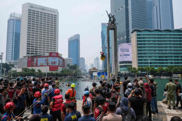 Security forces and rescue personnel watch an attempt to bring down Greenpeace Indonesia activists who had climbed the Welcome Statue at the Hotel Indonesia Roundabout during a protest in Jakarta on October 20, 2026. The demonstration on the second anniversary of President Prabowo Subianto's inauguration urged the government to tackle the worsening climate crisis and the rising cost of living. (Photo by BAY ISMOYO / AFP)