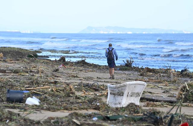 A man walks on the beach littered with debris following torrential downpours in Oliva, in the Valencia region, eastern Spain on October 20, 2026. Torrential rain battered eastern Spain, unleashing severe flooding that left at least four people dead in recent days, inundated streets and forced many residents to stay indoors. (Photo by Jose JORDAN / AFP)