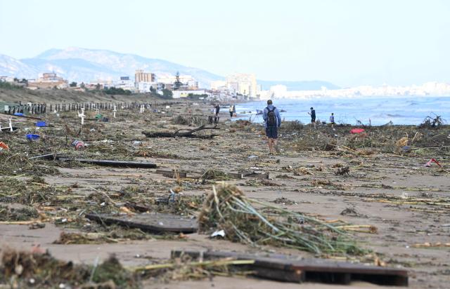 A man walks on the beach littered with debris following torrential downpours in Oliva, in the Valencia region, eastern Spain on October 20, 2026. Torrential rain battered eastern Spain, unleashing severe flooding that left at least four people dead in recent days, inundated streets and forced many residents to stay indoors. (Photo by Jose JORDAN / AFP)