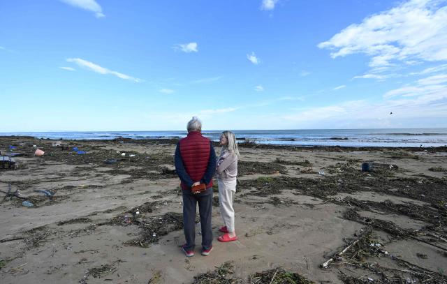 A couple stand on the beach littered with debris following torrential downpours in Oliva, in the Valencia region, eastern Spain on October 20, 2026. Torrential rain battered eastern Spain, unleashing severe flooding that left at least four people dead in recent days, inundated streets and forced many residents to stay indoors. (Photo by Jose JORDAN / AFP)