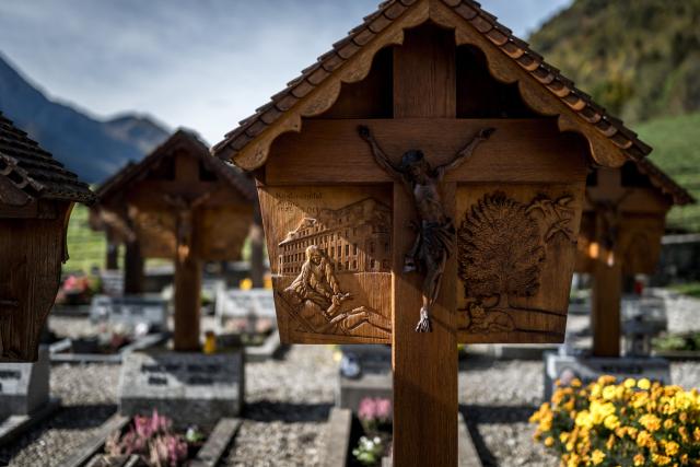 This photograph shows hand-carved wooden grave crosses in the cemetery of the Alpine village of Jaun, on October 19, 2026. Each cross features a sculpted bas-relief depicting the deceased person's profession, passion, or a significant aspect of their life, continuing a unique local tradition established by local woodworker Walter Cottier in 1948. On All Saints' Day, it is a longstanding tradition in Jaun to honor the deceased by gathering in reflection at graves adorned with these remarkable wooden sculptures. (Photo by Fabrice COFFRINI / AFP)