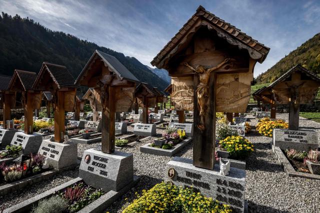 This photograph shows hand-carved wooden grave crosses in the cemetery of the Alpine village of Jaun, on October 19, 2026. Each cross features a sculpted bas-relief depicting the deceased person's profession, passion, or a significant aspect of their life, continuing a unique local tradition established by local woodworker Walter Cottier in 1948. On All Saints' Day, it is a longstanding tradition in Jaun to honor the deceased by gathering in reflection at graves adorned with these remarkable wooden sculptures. (Photo by Fabrice COFFRINI / AFP)