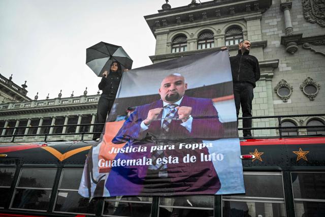 Two people hold a poster bearing a portrait of lawyer Francisco Solórzano Foppa during a posthumous tribute at Constitution Square in Guatemala City on October 20, 2026. A former Guatemalan prosecutor who denounced corruption cases and alleged links between gangs and politicians was shot dead in Guatemala City on October 17, 2026, police said. Lawyer Juan Francisco Solorzano Foppa was attacked at a football field he frequented on weekends, according to a police report, which said two suspected perpetrators had been detained on a preliminary basis. (Photo by Johan ORDONEZ / AFP)