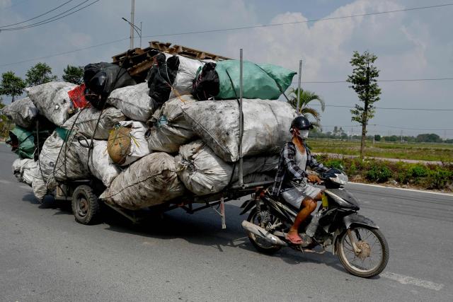 A man on a motorcycle pulls a cart loaded with bags of waste in Hanoi on October 21, 2026. (Photo by Nhac NGUYEN / AFP)