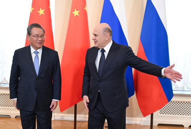 In this pool photograph distributed by the Russian state agency Sputnik, Russia's Prime Minister Mikhail Mishustin (R) welcomes Chinese Premier Li Qiang in Saint Petersburg on October 21, 2026. (Photo by Alexander Miridonov / POOL / AFP)