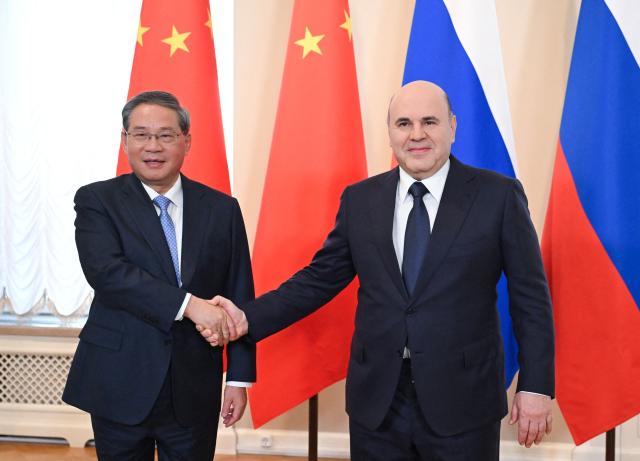 In this pool photograph distributed by the Russian state agency Sputnik, Russia's Prime Minister Mikhail Mishustin (R) shakes hand with Chinese Premier Li Qiang in Saint Petersburg on October 21, 2026. (Photo by Alexander Miridonov / POOL / AFP)