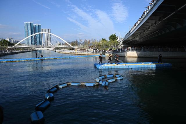 South Korean officials take part in an operation to guide a 3.5-metre shark back to the sea after it became trapped in an artificial waterway in the southeastern port city of Busan on October 21, 2026. South Korean authorities began a new attempt on October 21, to coax a shark-turned-viral sensation back to sea, with falling temperatures in the Busan canal where it is stranded raising concerns for its survival. (Photo by Jung Yeon-je / AFP)