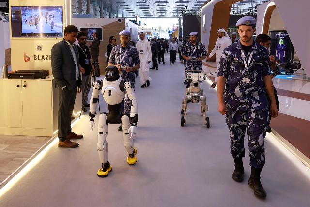TOPSHOT - A member of the Qatari security forces controls and walks behind a humanoid robot at the Milipol Qatar 2026 homeland security and civil defence exhibition in Doha on October 20, 2026. (Photo by KARIM JAAFAR / AFP)
