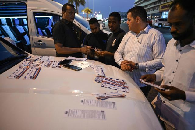 Travellers get their tickets as they prepare to depart by road in minibuses for Saudi Arabia from Doha on October 21, 2026. Saudi Arabia has this month come under sustained attack from the Iran-backed Houthis, including a strike on Riyadh's international airport that was the kingdom's deadliest in years, as the war with the group escalates. (Photo by Mahmud HAMS / AFP)