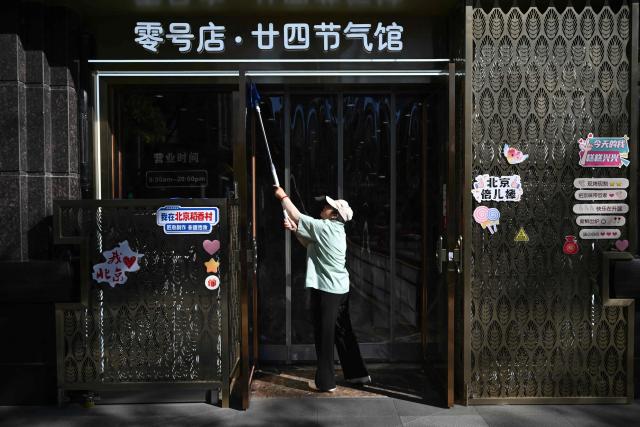 A worker cleans the entrance to a bakery in Beijing on October 21, 2026. (Photo by Pedro PARDO / AFP)