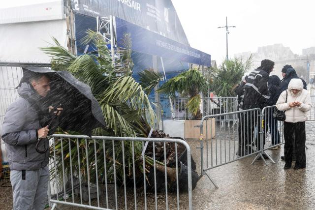 People wait under the rain in front of the entrance of the village of the Route du Rhum, which is closed due to weather conditions, in Saint-Malo, western France on October 21, 2026, a few days prior to the start of the 13th Route du Rhum - Destination Guadeloupe. From Saint-Malo in Brittany to Pointe-a-Pitre in Guadeloupe, over 100 skippers across 6 classes will take the start on November 1, 2026, in this solo transatlantic sailing race. (Photo by Sebastien Salom-Gomis / AFP)