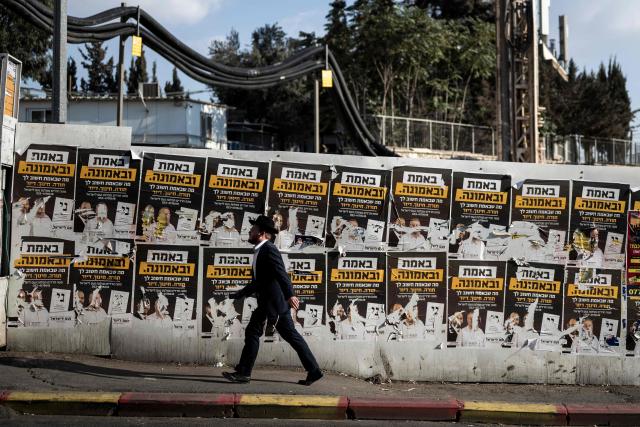 An ultra-Orthodox Jewish man walks past torn electoral posters on a wall along a street in Jerusalem on October 21, 2026, ahead of Israel's legislative election. Israel heads to the polls on October 27 in its first election since the October 7, 2023 Hamas-led attack, in what is seen as a referendum on the prime minister. (Photo by Jewel SAMAD / AFP)