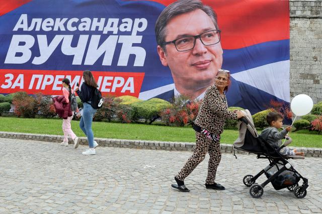 Pedestrians walk in front of a campaign banner showing Aleksandar Vucic, candidate for prime minister for the Serbian Progressive Party (SNS), ahead of an election campaign rally four days prior to the country's snap elections in Nis, Serbia, on October 21, 2026. The vote follows nearly two years of anti-corruption protests sparked by the November 2024 collapse of a railway station canopy in Novi Sad that killed 16 people and grew into a student-led movement demanding early elections. Aleksandar Vucic resigned as president on September 27 to lead the SNS election campaign and seek a return as prime minister. (Photo by Sasa DJORDJEVIC / AFP)