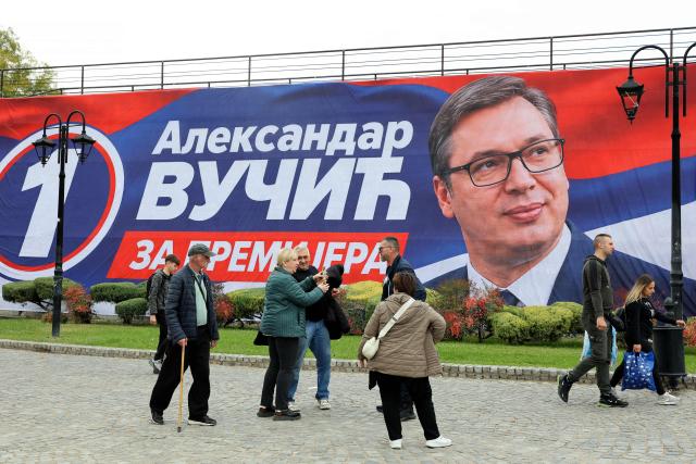 Pedestrians walk in front of a campaign banner showing Aleksandar Vucic, candidate for prime minister for the Serbian Progressive Party (SNS), ahead of an election campaign rally four days prior to the country's snap elections in Nis, Serbia, on October 21, 2026. The vote follows nearly two years of anti-corruption protests sparked by the November 2024 collapse of a railway station canopy in Novi Sad that killed 16 people and grew into a student-led movement demanding early elections. Aleksandar Vucic resigned as president on September 27 to lead the SNS election campaign and seek a return as prime minister. (Photo by Sasa DJORDJEVIC / AFP)