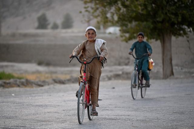 Afghan children ride bicycles along a street at Spin Ziarat village in the Dand district of Afghanistan's Kandahar province on October 21, 2026. (Photo by Sanaullah SEIAM / AFP)