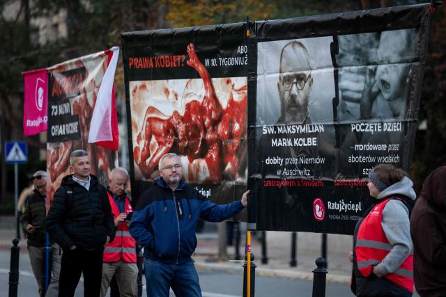 Pro-life activists hold anti-abortiona banners at a rally and rosary prayer organised by conservative groups opposed to loosening abortion laws in Poland, in front of the Polish Parliament in central Warsaw, as the banner in the background reads “Genocide”, on October 21, 2026. Poland's parliament voted on Tuesday to liberalise abortion laws in the traditionally Catholic country, which has some of the EU's most restrictive rules on ending pregnancies. (Photo by Wojtek RADWANSKI / AFP)