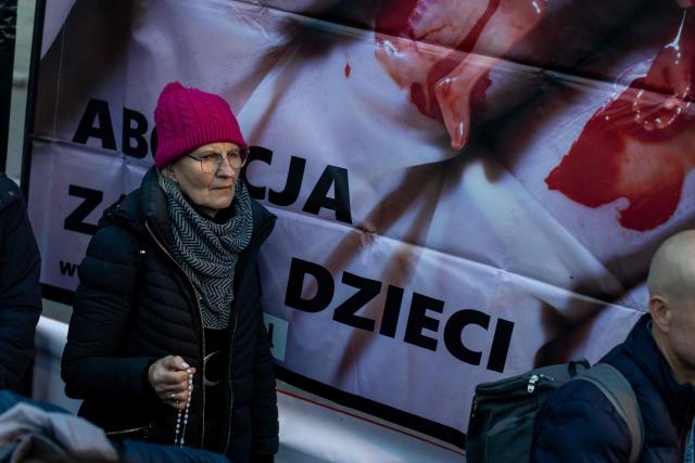Pro-life activists holds rosary at a rally and rosary prayer organised by conservative groups opposed to loosening abortion laws in Poland, in front of the Polish Parliament in central Warsaw, as the banner in the background reads “Genocide”, on October 21, 2026. Poland's parliament voted on October 20, 2026 to liberalise abortion laws in the traditionally Catholic country, which has some of the EU's most restrictive rules on ending pregnancies. (Photo by Wojtek RADWANSKI / AFP)