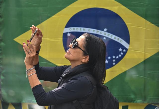 A woman takes pictures in front of  a Brazilian flag at Paulista Avenue in Sao Paulo, Brazil, on October 21, 2026.  (Photo by Juan BARRETO / AFP)