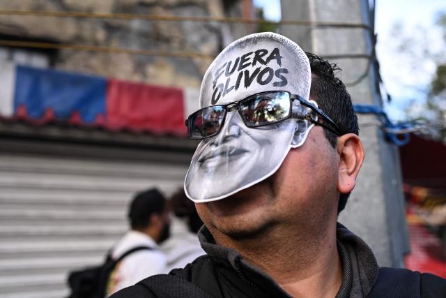 A worker from the Mexican Social Security Institute (IMSS) wears a mask bearing the slogan "Out Olivo," referring to a union leader, during a protest march demanding better wages and the provision of medicines for patients at hospitals across Mexico City on October 21, 2026. (Photo by Yuri CORTEZ / AFP)