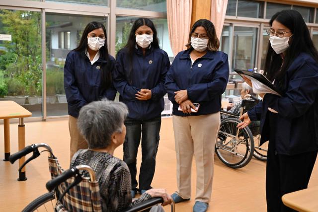 (From L-R) Ketsi Yahuarcani, Wendy Sangama, and Belen mayor Lina Arista Lopez, guests from Peru's Belen district, interact with a resident during a visit to a care-giving facility in Nanmoku village, Japan's Gunma prefecture on September 26, 2026. In a misty mountain village in Japan, residents recently welcomed unlikely guests from a Peruvian district along the Amazon River, seeing a chance to revive an ageing community facing extinction. Nanmoku village officials hope a sister-city agreement, which promotes cultural and people-to-people ties, will ultimately attract young people from Belen to live in Nanmoku, although how they might obtain residency remains unclear. (Photo by Rie KIKUCHI / AFP) / To go with AFP story Japan-Peru-social-population-demographics, FOCUS by Natsuko Fukue and Junior Raborg