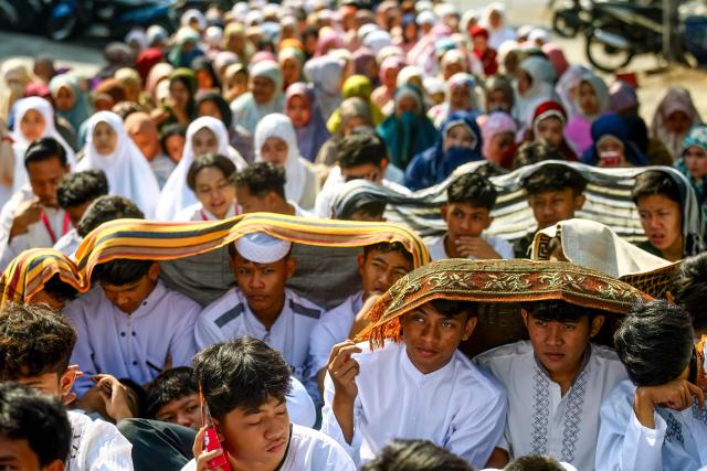 Students and residents shield themselves from the sun while participating in the Istisqa rain prayer gathering to pray for rain amidst a prolonged El Nino-induced drought in Malang, East Java province on October 22, 2026. (Photo by Hayu Yudha / AFP)