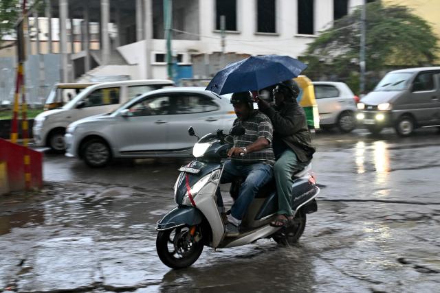 A scooterist shields themselves with an umbrella as they commute during rainfall in Bengaluru on October 22, 2026. (Photo by Idrees MOHAMMED / AFP)