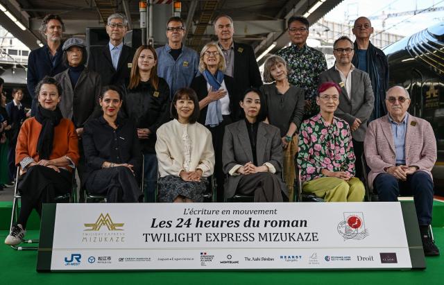 (From L, front) French novelist Muriel Barbery, French writer Claire Berest, Japanese writer Machi Tawara, Japanese writer Mariko Asabuki, Japanese author Anna Ogino, French writer Paul Fournel and (From L, middle) Japanese writer Hitonari Tsuji, Japanese novelist Hitomi Kanehara, "L'Ecriture en mouvement" Association Founder Anne Forrest-Wilson, Japanese author Kaori Ekuni, French poet Frederic Forte and (From L, rear) French writer Christophe Ono-dit-Biot, Japanese poet Hisaki Matsuura, Argentine writer Eduardo Berti, French writer Herve Le Tellier, Japanese author Toh EnJoe, French author Richard Collasse pose for a group photo at Shin-Osaka station in Osaka prefecture on October 22, 2026. Sixteen writers -- half French-speaking and half Japanese -- boarded a luxury train in Kyoto on October 22, 2026, faced with the unusual task of collectively writing a novel in under 24 hours. (Photo by Rie KIKUCHI / AFP) / To go with 'JAPAN-FRANCE-LITERATURE-TRANSPORT-TOURISM' Reportage by Julien GIRAULT