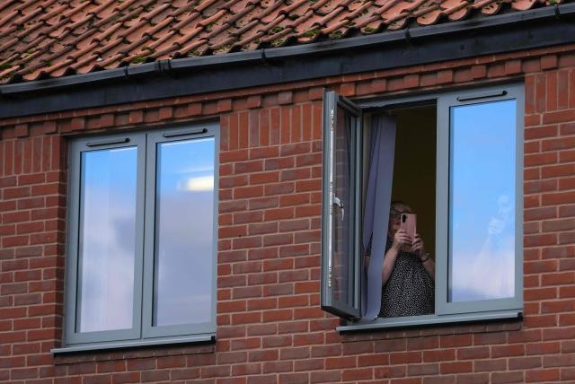 A person takes a photo from the window of an office as Britain's Catherine, Princess of Wales (unseen) greets well-wishers as she leaves after a visit to East Anglia's Children's Hospices' (EACH) shop in Hoveton, eastern England on October 22, 2026. Cafe 98, run by East Anglia's Children's Hospices (EACH), is the charity's first and only cafe, forming part of EACH's fundraising operation and serving as a community hub for local residents. (Photo by Ben Stansall / POOL / AFP)