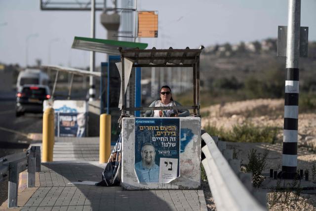 An Israeli settler stands next to electoral posters as she waits for transportation in Gush Etzion, in the Israeli-occupied West Bank, on October 22, 2026, ahead of Israel's legislative election. Israel heads to the polls on October 27 in its first election since the October 7, 2023 Hamas-led attack, in what is seen as a referendum on the prime minister. (Photo by Jewel SAMAD / AFP)