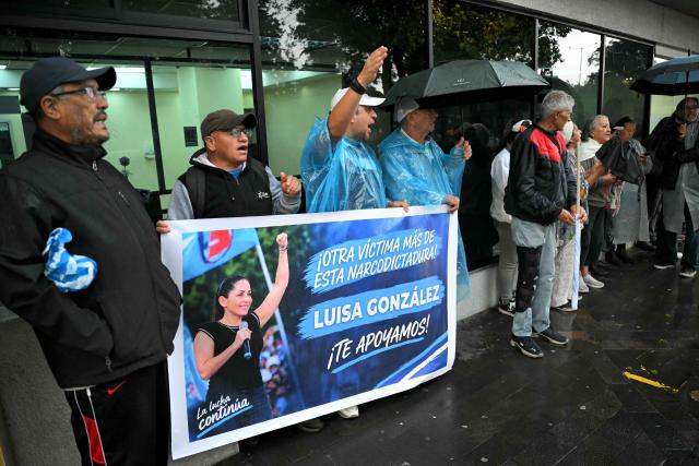 Supporters of former Ecuadorian presidential candidate Luisa Gonzalez hold a banner reading "Another victim of this narco-dictatorship. Luisa Gonzalez, we support you" outside the Flagrancy Unit in Quito on October 22, 2026, following her arrest. Ecuador's opposition on October 22, 2026, accused US-backed President Daniel Noboa of running a "dictatorship" following the arrest of former presidential candidate Luisa Gonzalez, the latest left-wing figure to face legal proceedings. (Photo by Rodrigo BUENDIA / AFP)