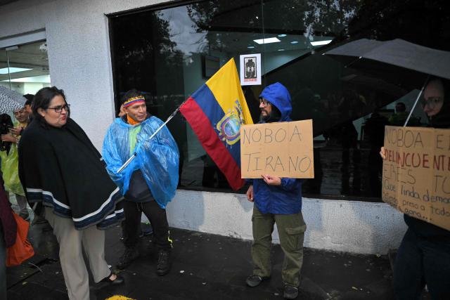 A supporter of former Ecuadorian presidential candidate Luisa Gonzalez holds a placard reading "Noboa tyrant" as another supporter holds an Ecuadorian flag outside the Flagrancy Unit in Quito on October 22, 2026, following her arrest. Ecuador's opposition on October 22, 2026, accused US-backed President Daniel Noboa of running a "dictatorship" following the arrest of former presidential candidate Luisa Gonzalez, the latest left-wing figure to face legal proceedings. (Photo by Rodrigo BUENDIA / AFP)