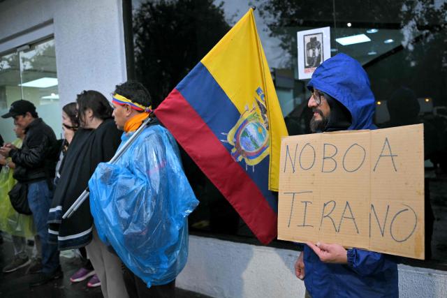 A supporter of former Ecuadorian presidential candidate Luisa Gonzalez holds a placard reading "Noboa tyrant" as another supporter holds an Ecuadorian flag outside the Flagrancy Unit in Quito on October 22, 2026, following her arrest. Ecuador's opposition on October 22, 2026, accused US-backed President Daniel Noboa of running a "dictatorship" following the arrest of former presidential candidate Luisa Gonzalez, the latest left-wing figure to face legal proceedings. (Photo by Rodrigo BUENDIA / AFP)