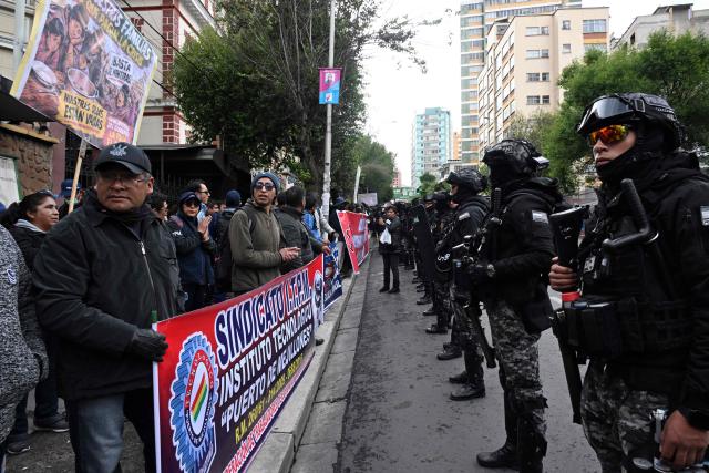 Teachers stand behind banners facing a line of riot police during a march to protest the government's economic and educational policies in La Paz on October 22, 2026. (Photo by Aizar RALDES / AFP)