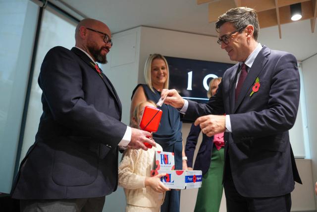 British Army veteran Steven Knighton holds a collection tin as Britain's Prime Minister Andy Burnham donates to the Poppy Appeal on October 22, 2026 in Manchester, northern England. Ahead of Remembrance Day. (Photo by Christopher Furlong / POOL / AFP)