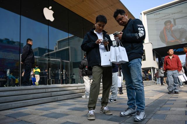 Two men use phones after shopping at an Apple as the iPhone Duo goes on sale in China, in Beijing on October 23, 2026. (Photo by WANG Zhao / AFP)