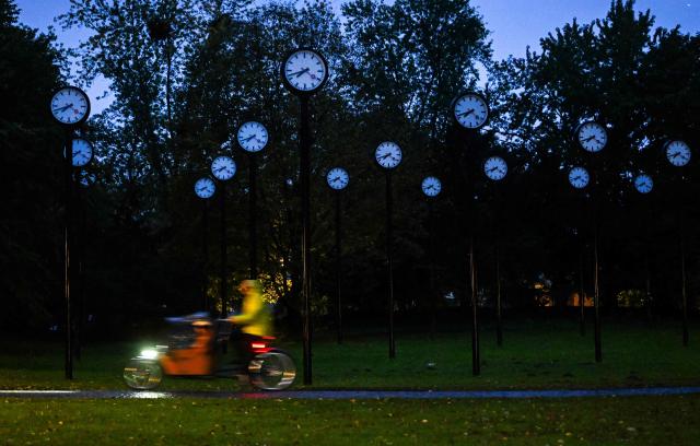 A man rides his bike in front of clocks of the art installation 'Zeitfeld' (time field) by German artist Klaus Rinke in Duesseldorf, western Germany, on October 23, 2026. Daylight Saving Time will end on October 25, 2026, and clocks will be turned one hour backward for winter time. (Photo by Ina FASSBENDER / AFP)