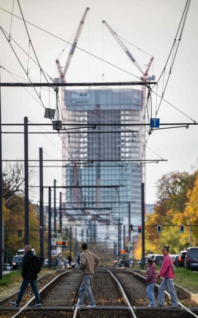 People cross tramway tracks at Berlin's Prenzlauer Allee as construction work on the Covivio tower at Alexanderplatz (background) continues on October 23, 2026. (Photo by John MACDOUGALL / AFP)