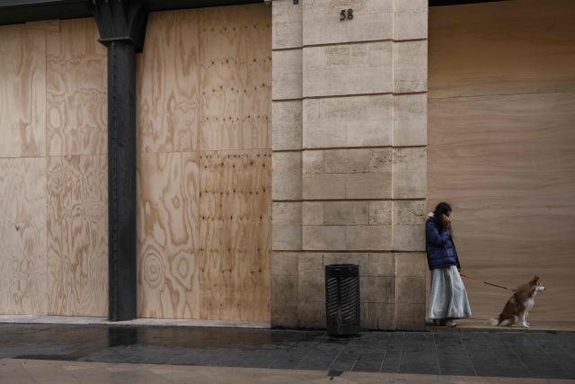 A woman with a dog speaks on her phone in front of boarded-up shops ahead of a demonstration planned for October 24, in central Bordeaux, southwestern France, on October 23, 2026. (Photo by Philippe LOPEZ / AFP)