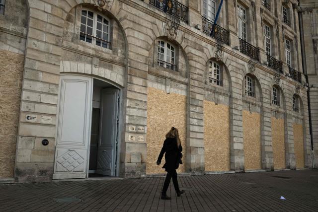 A woman walks past the boarded-up ground-floor windows of a historic building ahead of a demonstration planned for October 24, in central Bordeaux, southwestern France, on October 23, 2026. (Photo by Philippe LOPEZ / AFP)