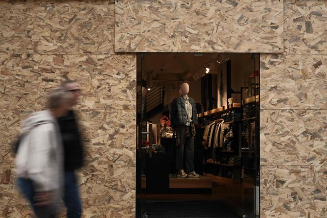 Pedestrians walk past a clothing store whose entrance is framed by protective wooden panels ahead of a demonstration planned for October 24, in central Bordeaux, southwestern France, on October 23, 2026. (Photo by Philippe LOPEZ / AFP)