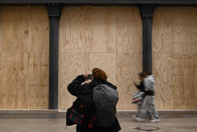A passer-by takes a picture of a boarded-up shop ahead of a demonstration planned for October 24, in central Bordeaux, southwestern France, on October 23, 2026. (Photo by Philippe LOPEZ / AFP)