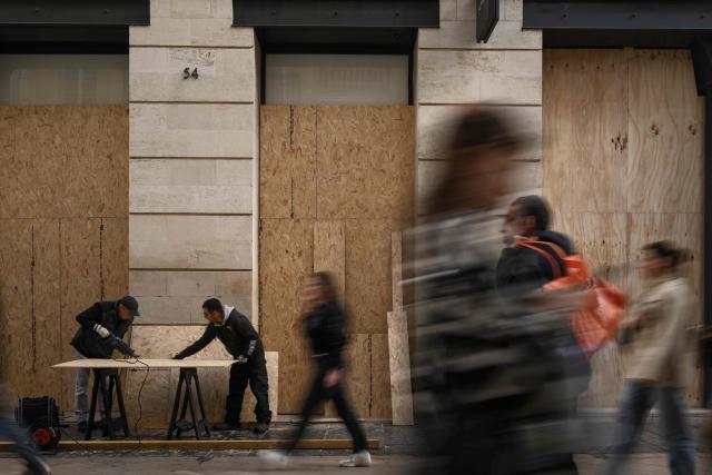 Pedestrians walk past workers cutting wooden panels to board up shops ahead of a demonstration planned for October 24, in central Bordeaux, southwestern France, on October 23, 2026. (Photo by Philippe LOPEZ / AFP)