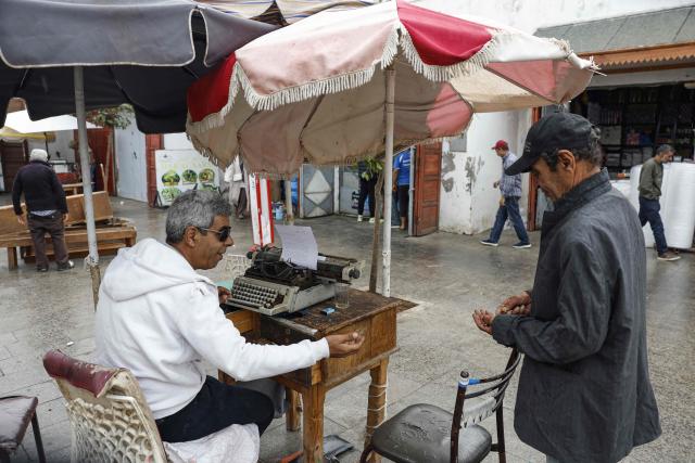 A man offering public typing and writing services uses a traditional typewriter at Bab El Had Square in Rabat, near the entrance to the medina on October 22, 2023. Street typewriting persists in Rabat as public writers provide customers with bureaucratic drafting and formatting of administrative documents. (Photo by Abdel Majid BZIOUAT / AFP)