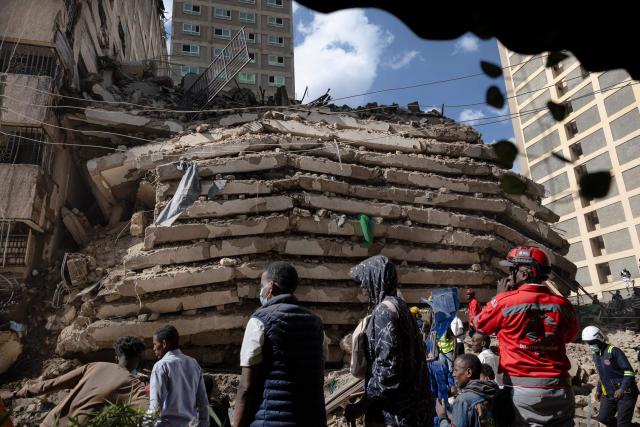 People gather at the site of a collapsed building as floor slabs lie piled up in the rubble of a residential building that crumbled as it was still under construction in the Eastleigh neighborhood of Nairobi on October 23, 2026. A multi-storey building collapsed mid-construction in the Kenyan capital on October 23, the Red Cross said, with reports from local media of casualties and looting at the site. Videos spreading online showed a dramatic crash and huge clouds of dust as the building came down in a busy business and residential district. (Photo by Tony KARUMBA / AFP)
