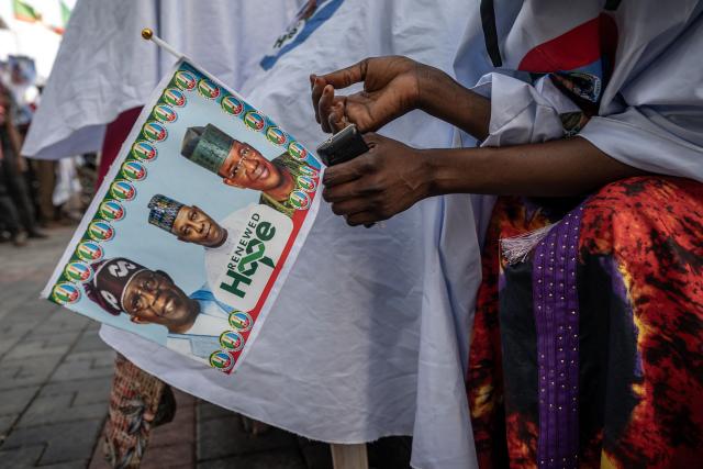 A supporter holds an All Progressives Congress (APC) campaign flag outside a party builingin Kaduna, on October 23, 2026, ahead of the presidential campaign flag-off rally. Nigerian President Bola Tinubu launches his re-election campaign on Saturday facing voter anger over insecurity and economic hardships. (Photo by Light Oriye Tamunotonye / AFP)