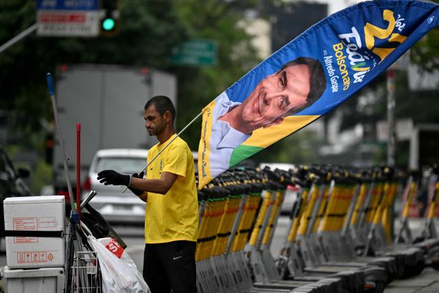 A man carries a banner bearing a picture of Brazil's right-wing senator and Liberal Party (PL) presidential candidate Flavio Bolsonaro in Sao Paulo, Brazil, on October 23, 2026. Brazil's President Lula da Silva and right-wing senator Flavio Bolsonaro head to a runoff election on October 25, a race that has become mired in allegations of social media malfeasance. (Photo by Juan BARRETO / AFP)